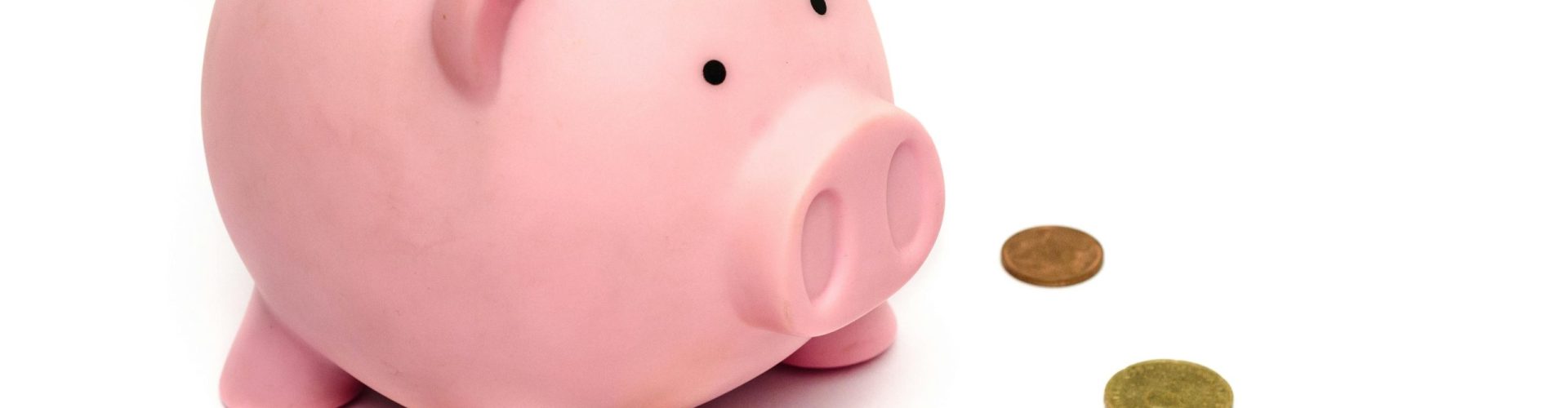 A pink piggy bank surrounded by scattered coins, symbolizing savings and financial investment.