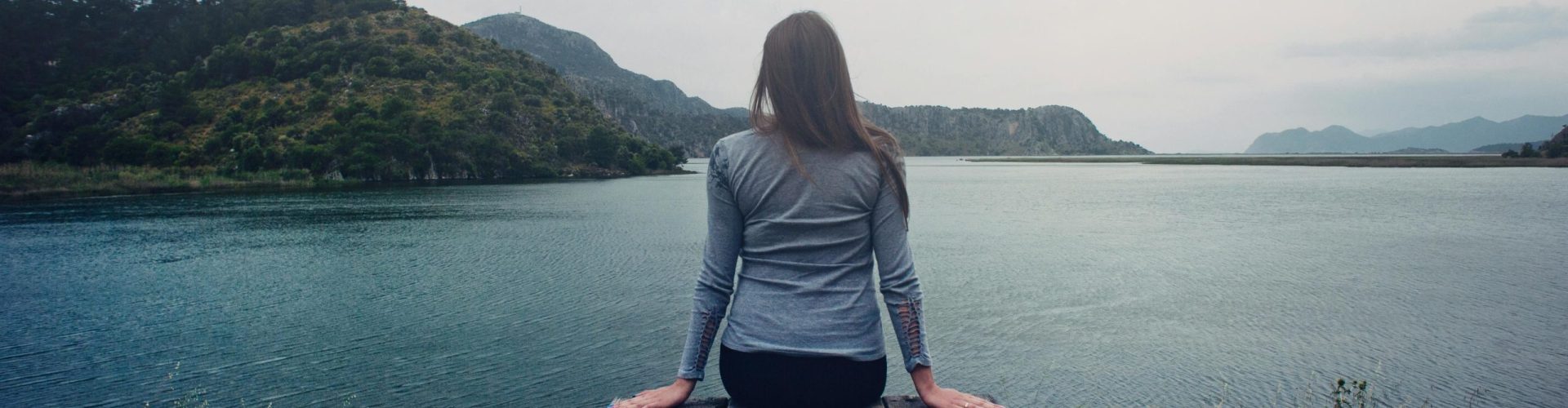 A woman sitting on wooden planks, enjoying a serene mountain lake view.
