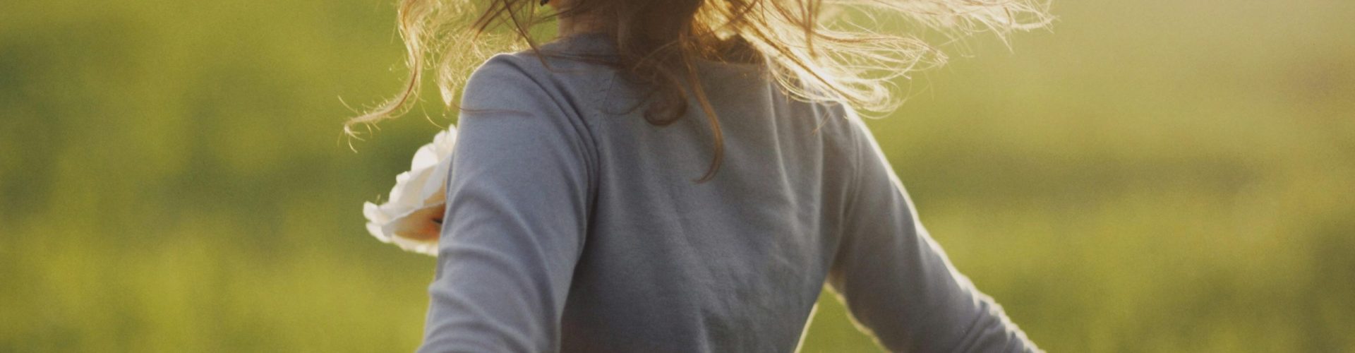 Joyful woman dancing freely in a sunlit field, embracing nature's beauty.