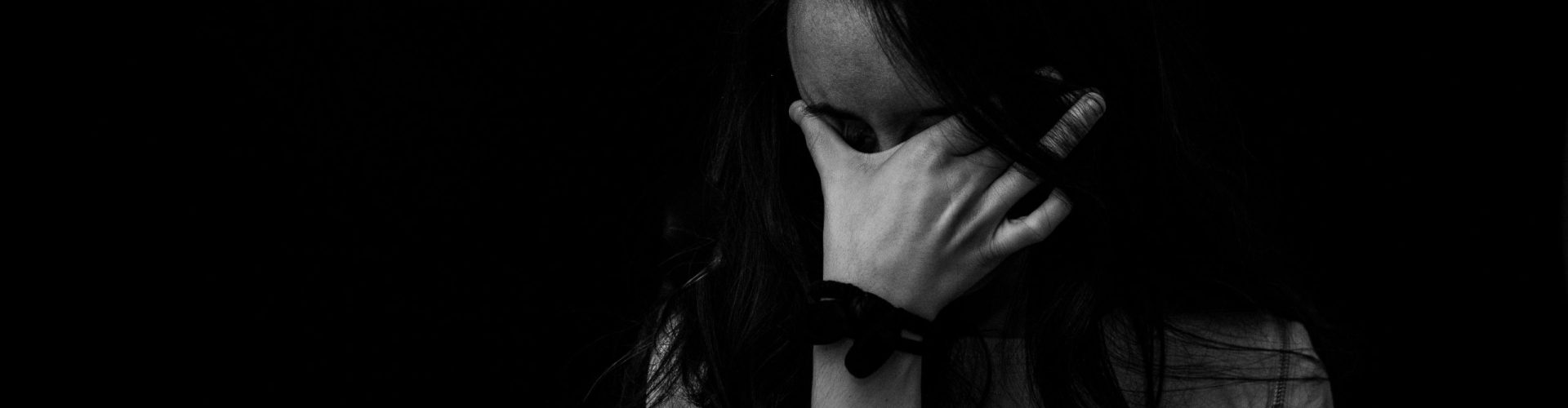Intense black and white portrait capturing the emotion and introspection of a woman covering her face.