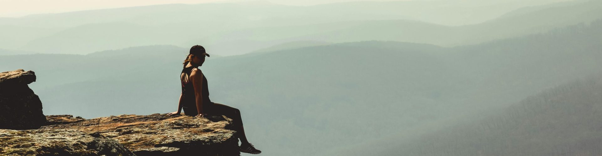 Woman sitting on a cliff edge overlooking a vast mountain landscape in Arkansas.