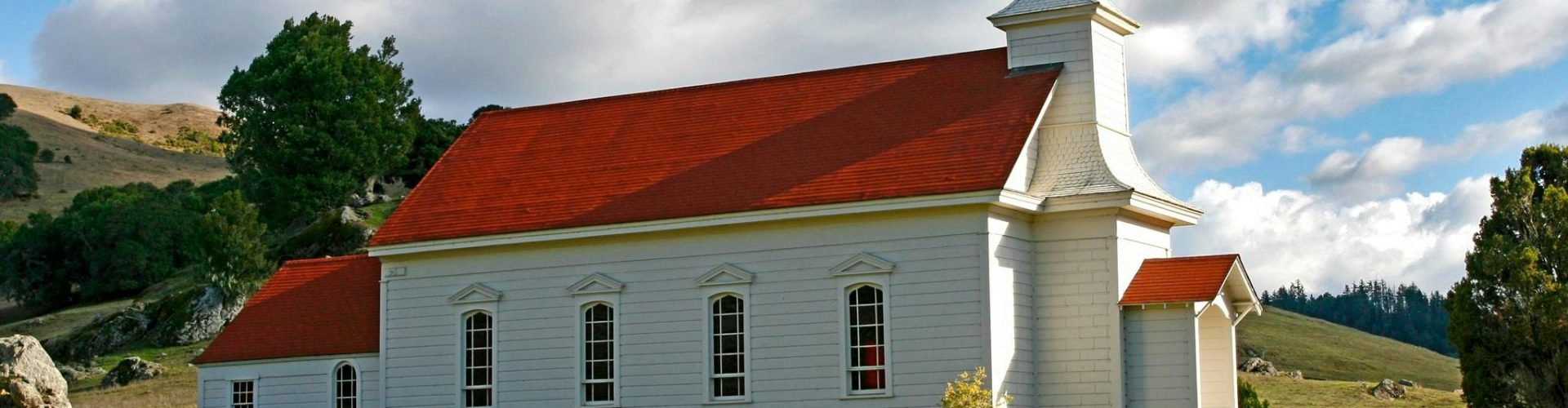 Charming rural church with red roof and steeple against a picturesque countryside backdrop.