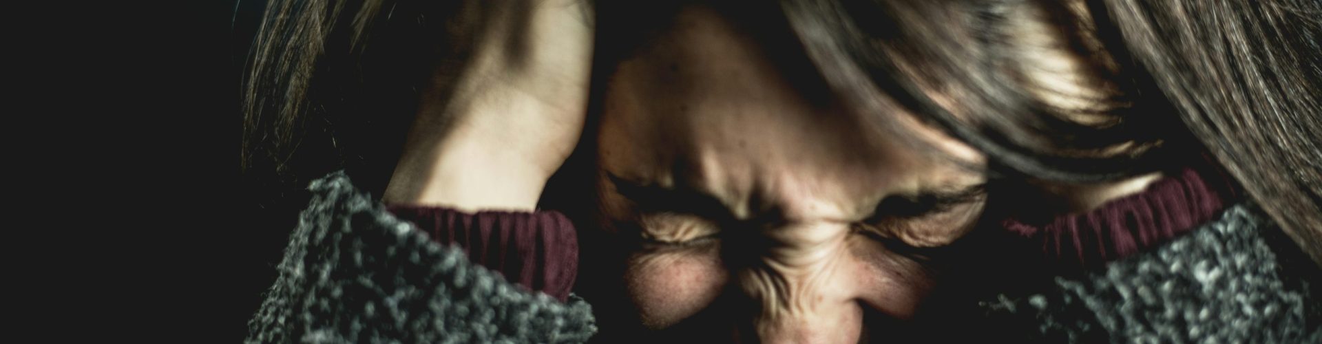 Close-up of a woman in distress with eyes closed and hands in hair, expressing anxiety.