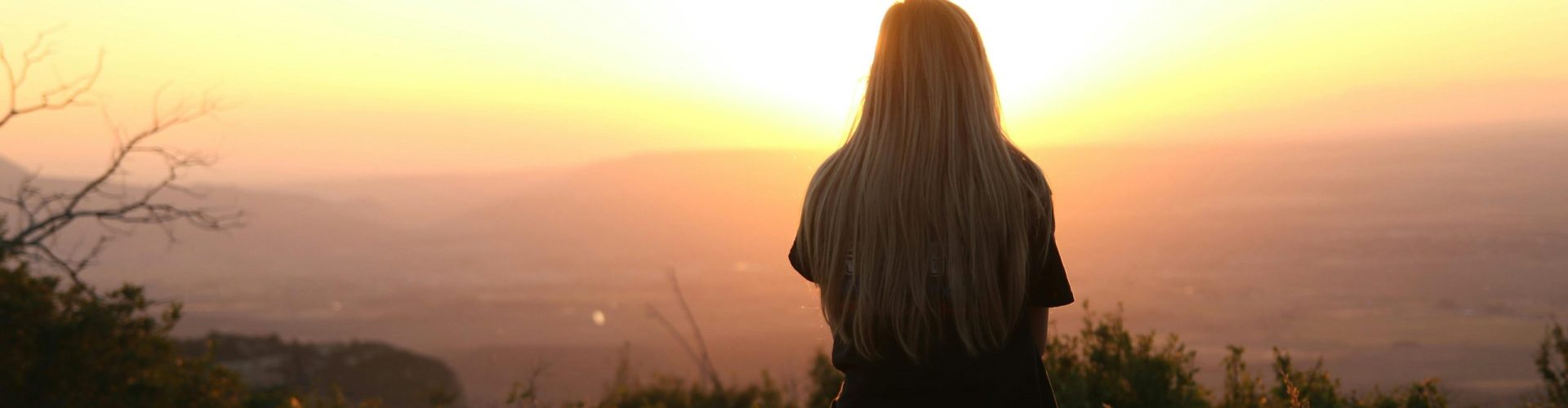 Woman sitting in nature, watching sunset over fields. Peaceful and serene outdoor scene.