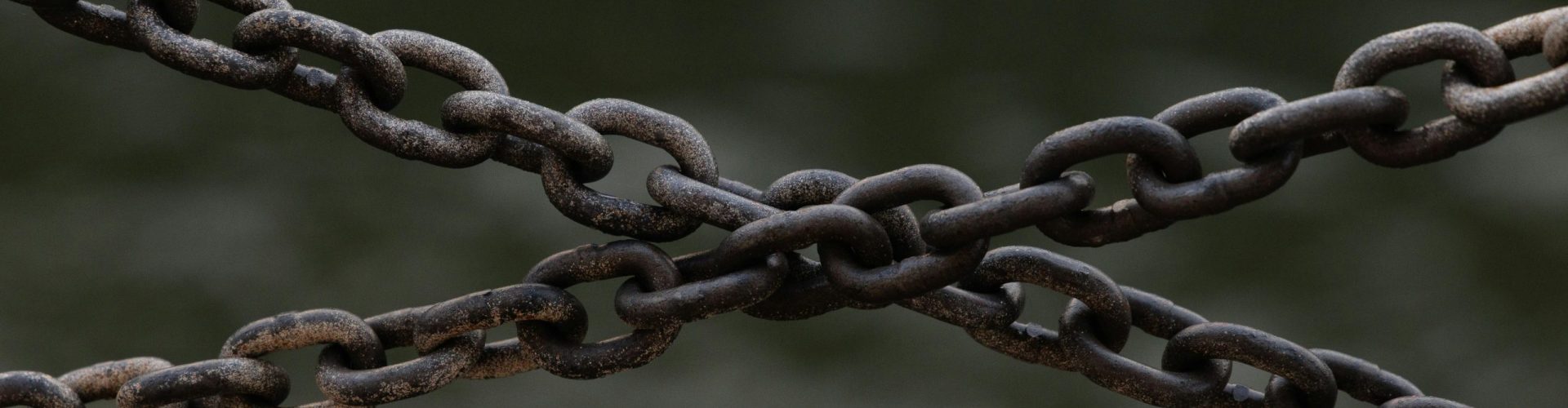 Close-up of crossed rusty chains over a blurred green background.