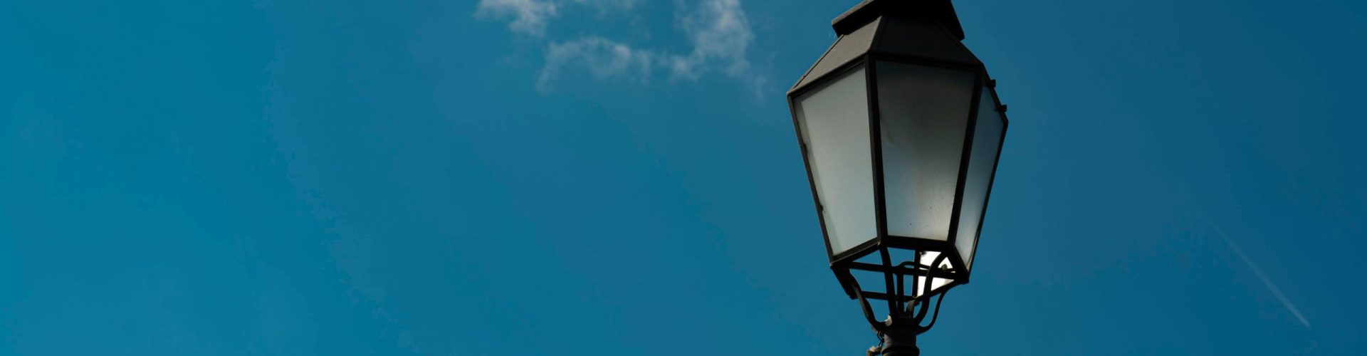 A classic street lamp silhouetted against a bright blue sky with fluffy clouds.