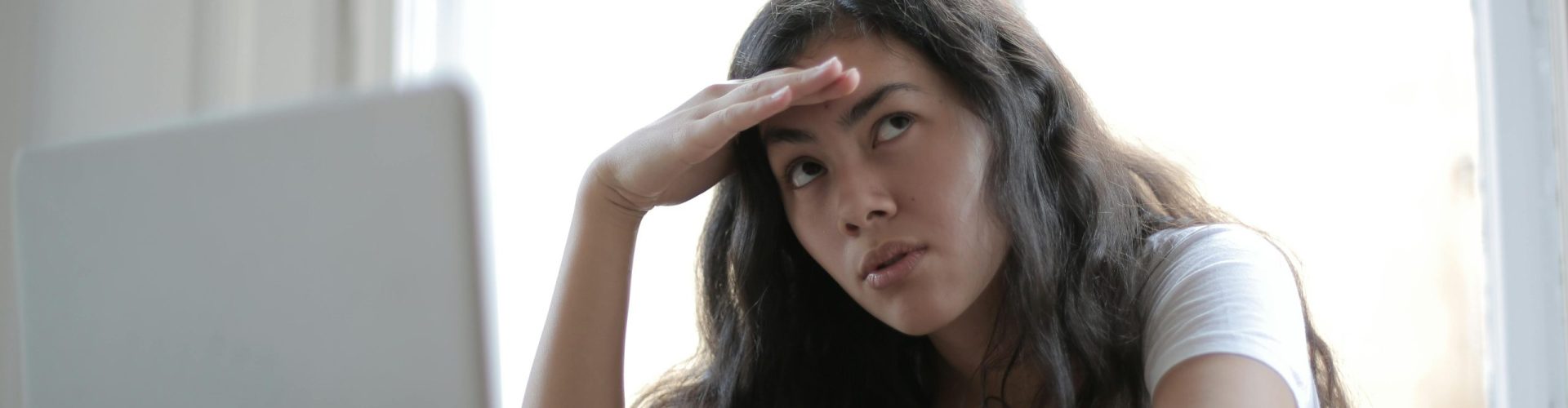 Irritated ethnic female entrepreneur in casual wear sitting at table with netbook and touching head while waiting for internet connection during remote work
