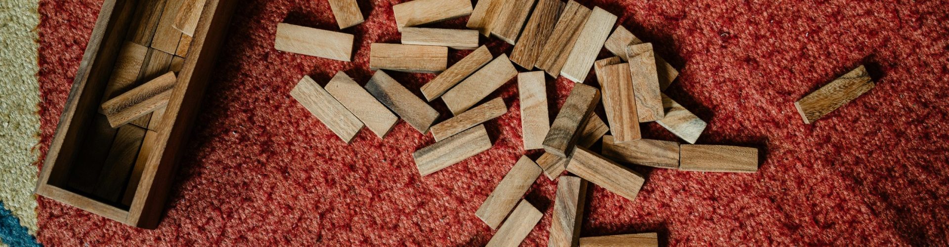 Top view of wooden box and pile of blocks for playing in jenga tower game arranged on floor carpet