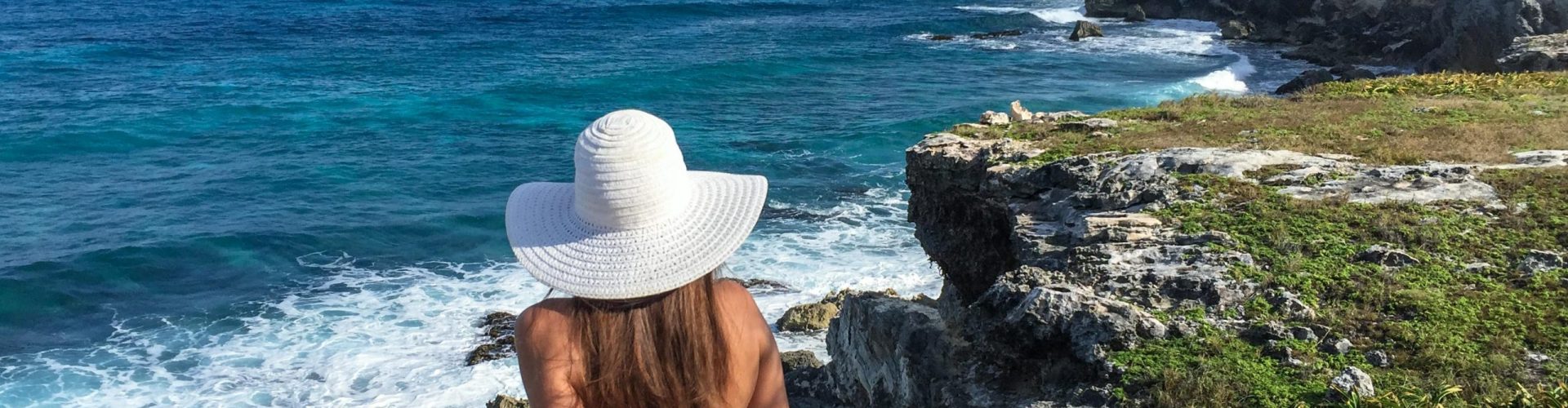 A woman in a white sun hat enjoys a scenic ocean view from a cliff on Isla Mujeres.