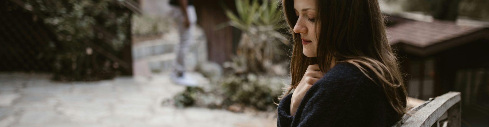 A woman sitting alone on a bench with a distant person, evoking a contemplative mood.
