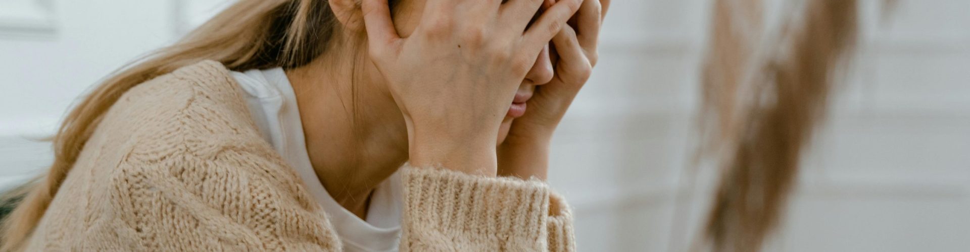 A woman sitting indoors covering her face in frustration, depicting stress and mental health challenges.