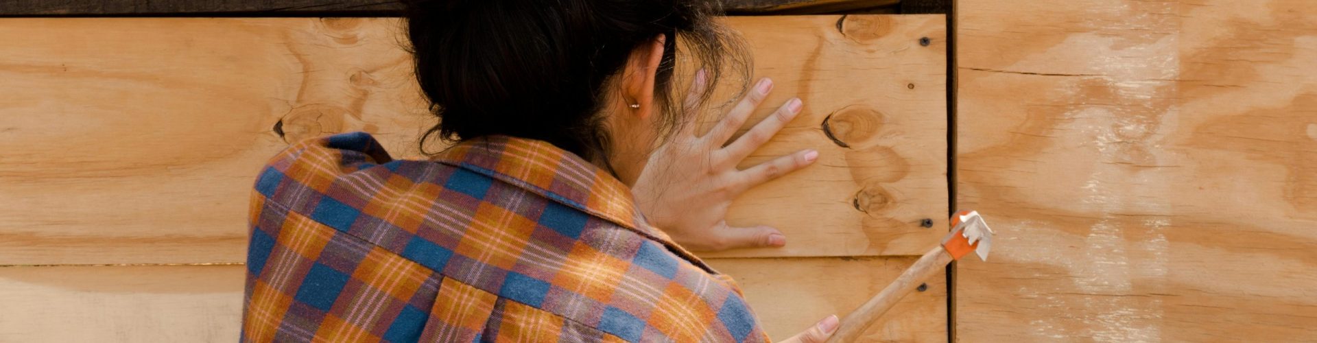 A woman in a plaid shirt expertly hammering a wooden plank. Empowerment in carpentry.