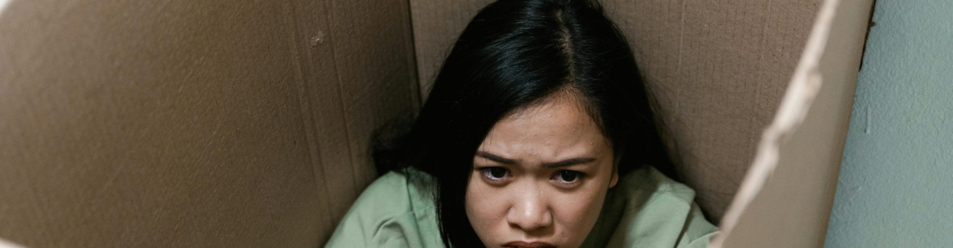 A woman inside a cardboard box symbolizes feelings of anxiety and claustrophobia.