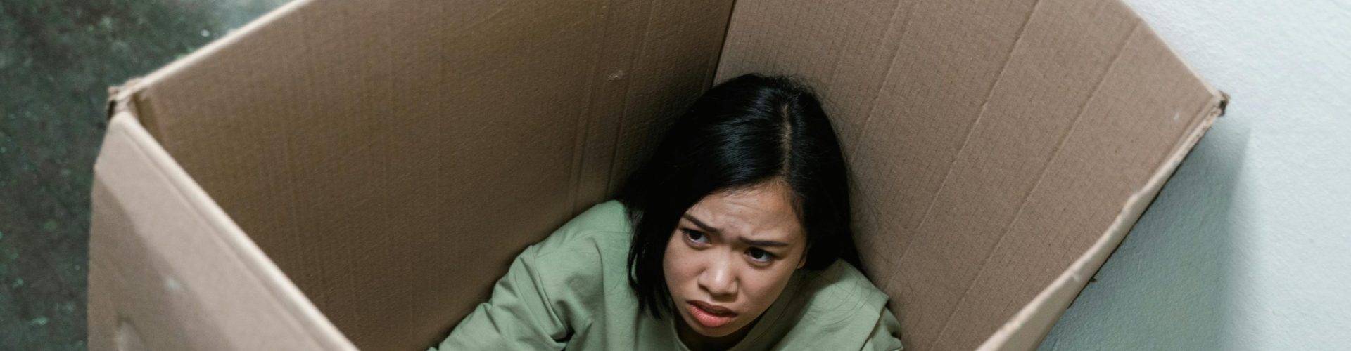 Woman in a cardboard box, symbolizing feelings of anxiety and claustrophobia.