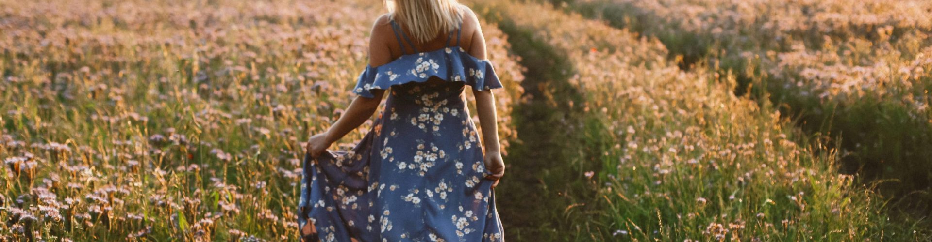 A woman walking in a floral dress through a bright flower field during sunset, showcasing tranquility and nature.