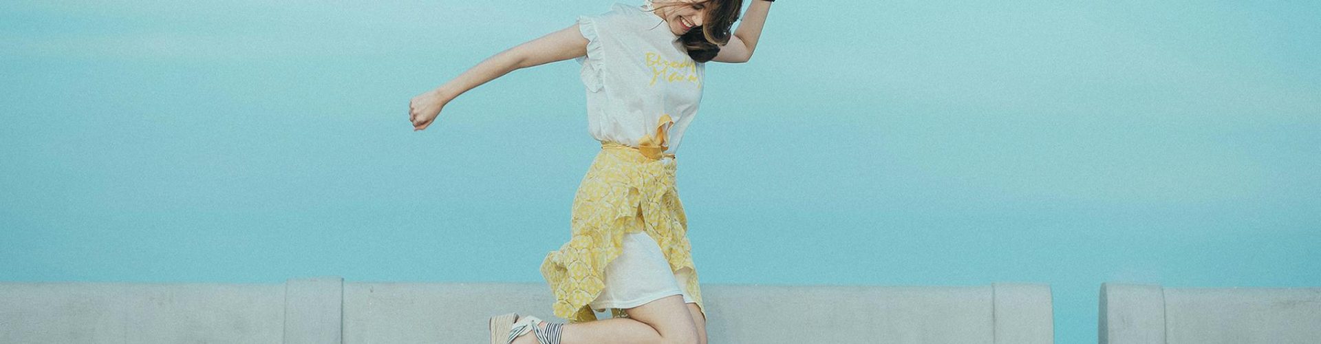 Woman jumping cheerfully on a bridge under a sunny blue sky, embodying freedom and happiness.